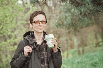 Short-haired woman with glasses holds a reusable silicone mug in hand. Camping, hiking, sustainable consumption.