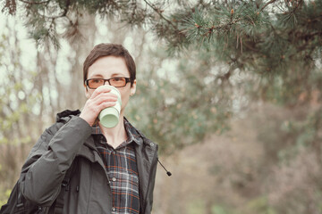 Short-haired woman in glasses drinks from reusable silicone mug. Camping, hiking, sustainable consumption.
