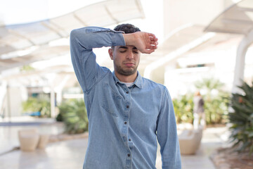 young handsome man looking stressed, tired and frustrated, drying sweat off forehead, feeling...