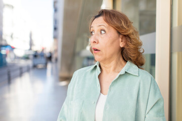 middle age woman feeling shocked and surprised, looking to copy space on the side with amazed, open-mouthed look