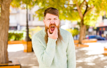 red hair bearded man with mouth and eyes wide open and hand on chin, feeling unpleasantly shocked, saying what or wow