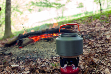Fototapeta premium Tourist gas kettle on the background of live fire. Camping with a gas kettle. a kettle boiling on a camping stove to make tea while hiking