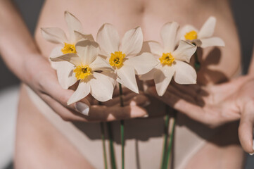 A woman holds daffodils in her hands close-up. The girl's hands cover her panties and underwear...