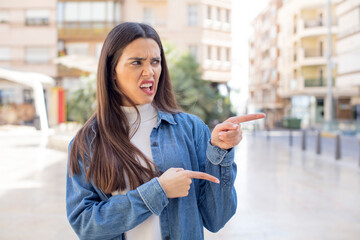 pretty young adult woman feeling shocked and surprised, pointing to copy space on the side with amazed, open-mouthed look