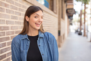 young pretty woman looking happy and friendly, smiling and winking an eye at you with a positive...