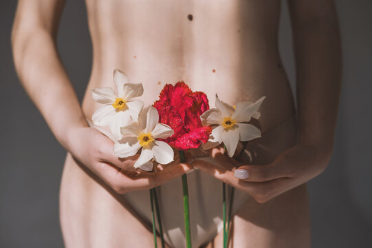 A woman holds daffodils and a red tulip in her hands close-up. The girl's hands cover the intimate areas with flowers - a symbol of innocence. Symbolic image of menstruation