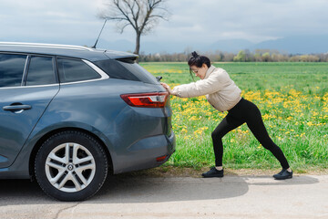 A woman pushing a broken-down car outside.