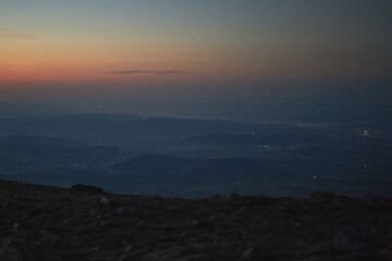 Mountains at sunrise. Natural mountain landscape with illuminated misty peaks, foggy slopes and valleys, blue sky with orange yellow sunlight