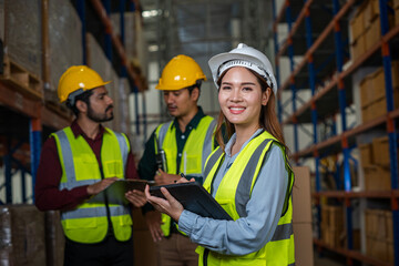 Warehouse employees reading a clipboard ann checking packages on shelf in a large logistics centre.