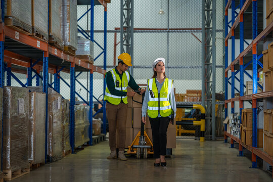 Warehouse employees reading a clipboard ann checking packages on shelf in a large logistics centre.