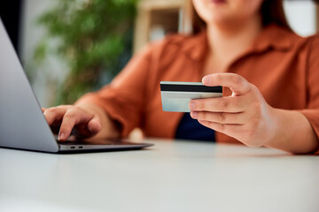 A close-up of a woman holding a credit card and shopping online over the laptop.