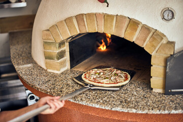 Male worker putting a pizza in the oven with a fireplace, pizza on the shovel.