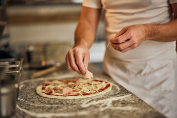 Close-up of a male hands, making pizza, putting a ham on the pizza dough.