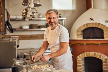 Portrait of a smiling male pizza master, posing for the camera while making pizzas.