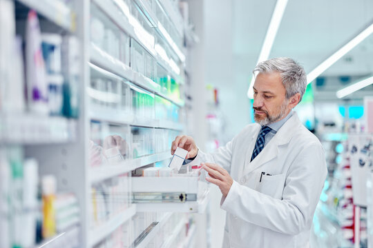 Side view of a male pharmacist taking a box of medicine from the drawer.