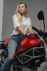 Obraz na płótnie Canvas Studio shot of blond haired woman weared in shirt and jeans riding red colored motorbike.