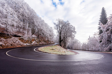 A curved road in forest in Krusne Hory during winter fogy day.