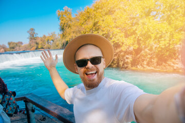 Happy tourist man in hat holds an action camera and takes selfie background waterfall Antalya, Turkey