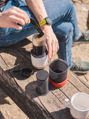 Man making AeroPress coffee on a beach. AeroPress Go coffee. Outdoor coffee.  