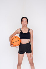 A sporty and athletic young woman posing while holding basketball on the side with one hand. Isolated on a white background.