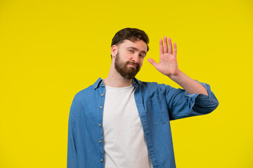 Hello Hi Young cheerful handsome bearded man greeting with open hand, enjoying communication, isolated on yellow background. close up portrait, body language.