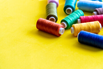  Spools of thread for sewing of various colors, on a yellow background with space for text.