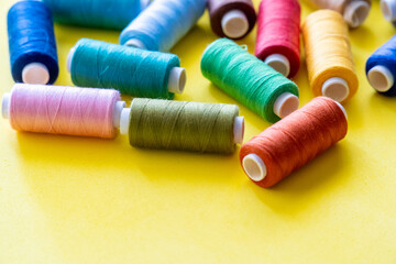  Spools of thread for sewing of various colors, on a yellow background with space for text.