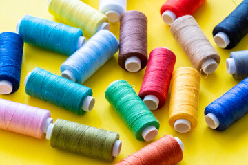  Spools of thread for sewing of various colors, on a yellow background, top view.