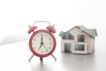 House model with alarm clock on wooden background.