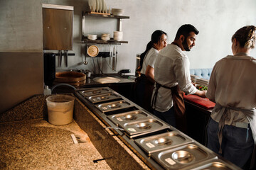 Back view of three concentrated multinational chefs prepare healthy food in kitchen