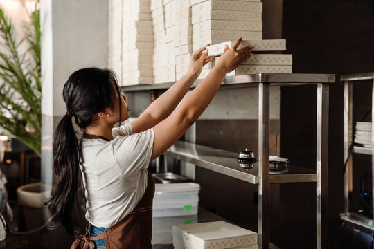 Side View Of Confident Busy Asian Female Chef Stacking Boxes In Kitchen