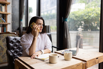 Young Caucasian business woman with long brunette hair working on laptop in cafe. College student using technology , online education, freelance 