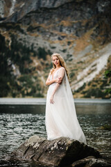The bride on the stony shore near the lake in the mountains. Wedding on a backdrop of mountain landscape. Scenic mountain view.