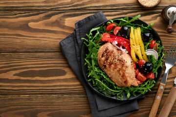 Salad with grilled chicken breas fillet with fresh arugula, tomatoes and olives on black plate on old wooden dark background. Chicken meat with salad. Ketogenic lunch. Healthy food. Top view.