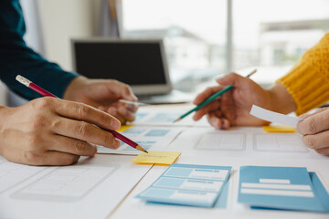 Close up ux developer and ui designer brainstorming about mobile app interface wireframe design on table with customer breif and color code at modern office.Creative digital development agency