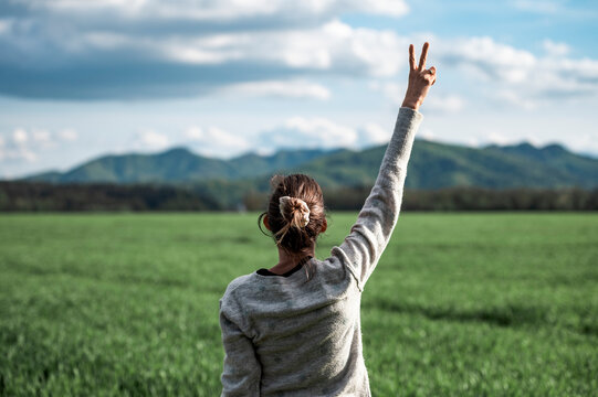A woman standing in beautiful green meadow or field with her arm raised high in a victory gesture