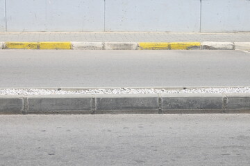A street border painted in white and black on the background of the road and green foliage in the summer closeup. Road safety, minimalism.