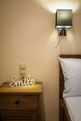 Bedroom interior details in pastel colors. Part of bed with pillows and bedside table with decorative word SMILE. Vertical photo. 