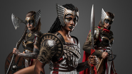 Studio shot of three amazons with makeup and armour against grey background.