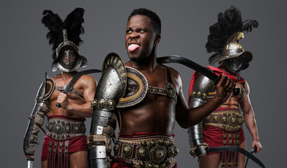 Portrait of mad african gladiator from past with paired swords and two comrades.