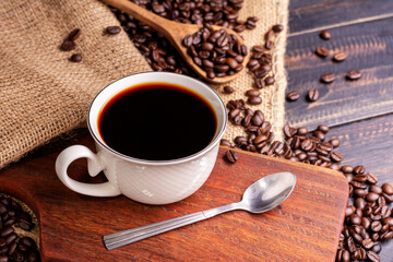 Freshly brewed coffee. Coffee cup or mug arranged on a black wooden table with roasted coffee beans. Espresso mocha cappuccino barista on dark background - top view