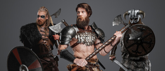 Shot of savage vikings from antique north with axes against gray background.