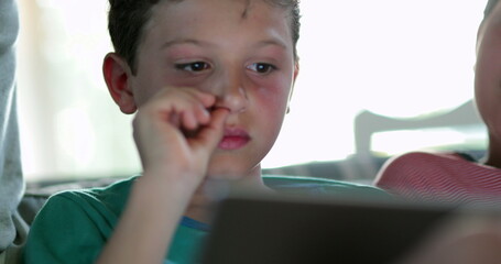 Candid child using tablet scratching face