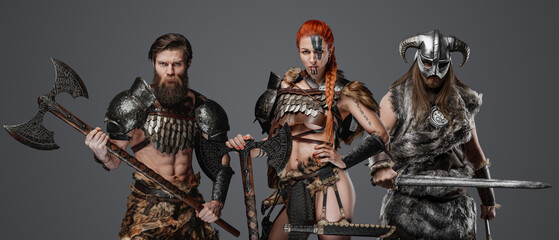Shot of nordic amazon with red hairs with two fierce comrades with armour and axes.
