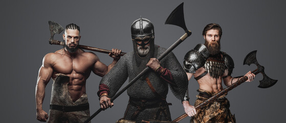 Studio shot of old man viking with two barbarians against gray background.