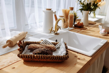 Fresh bread and utensils on the kitchen table, ready to be cooked. Simple modern scandinavian style kitchen, kitchen details, wooden table, bouquet of flowers in a vase on the table. - obrazy, fototapety, plakaty