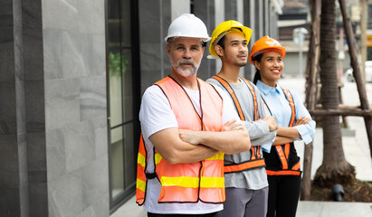 Unity and teamwork concept. Architect contractor senior man and team engineering standing together in construction site. Professional construction civil engineer team