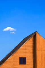 Glass attic window on wooden gable roof of vintage house against blue sky in minimal style and...
