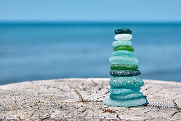Balanced pyramid of sea-polished glass bottle shards on a weathered wooden surface against the...
