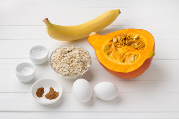 Ingredients for pumpkin pancakes with oatmeal and banana: pumpkin, banana, oatmeal, eggs, spices, salt, baking powder on a white background. Cooking delicious vegetarian food